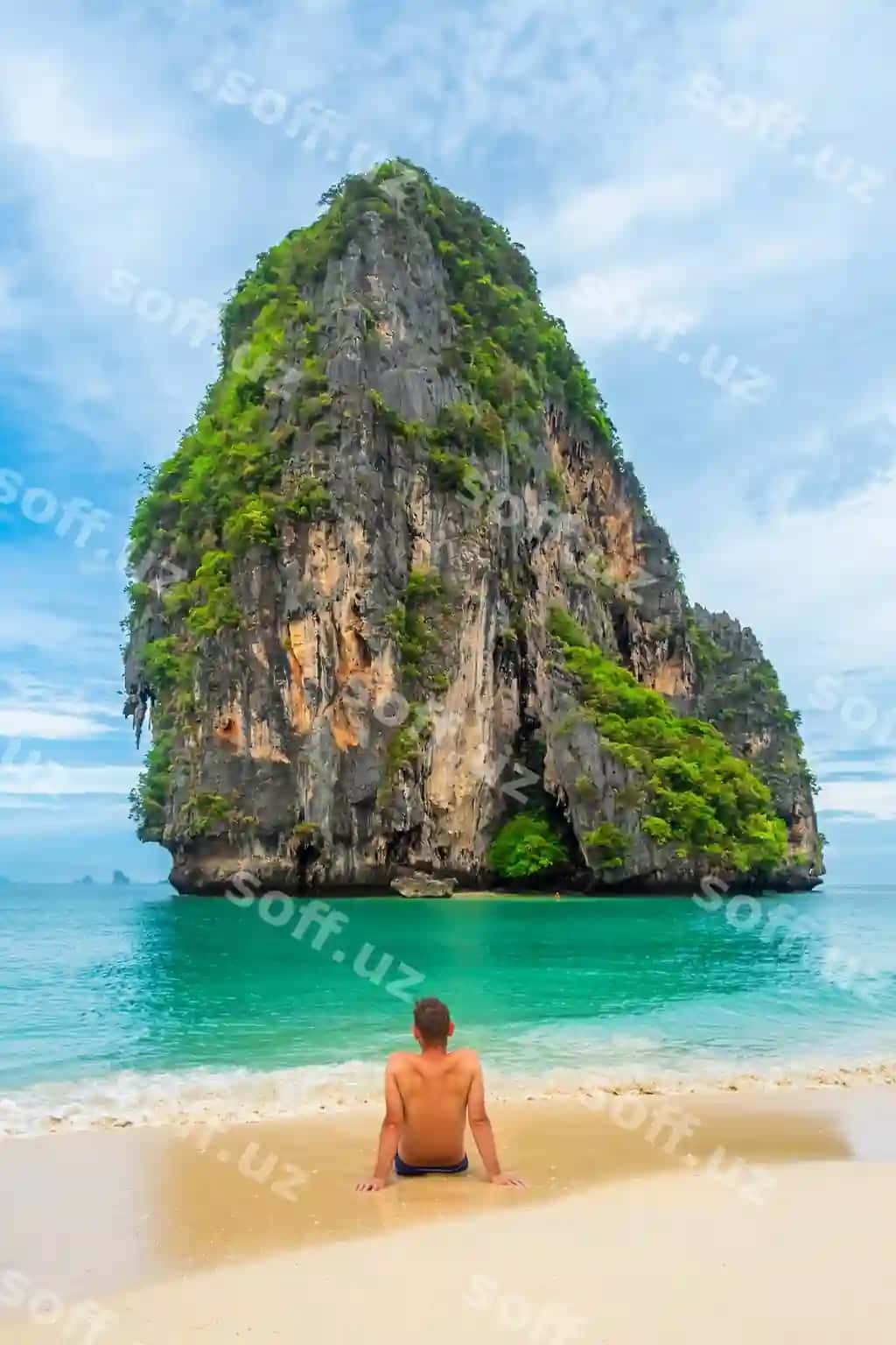 Sayyoh Phra Nang qumli poyintaqasida o'tirgan, Railay Bay Krabidagi qora nok toshli orolni qaraydi. | Man tourist sits phra nang sandy beach looking ko rang nok rocky island railay bay krabi