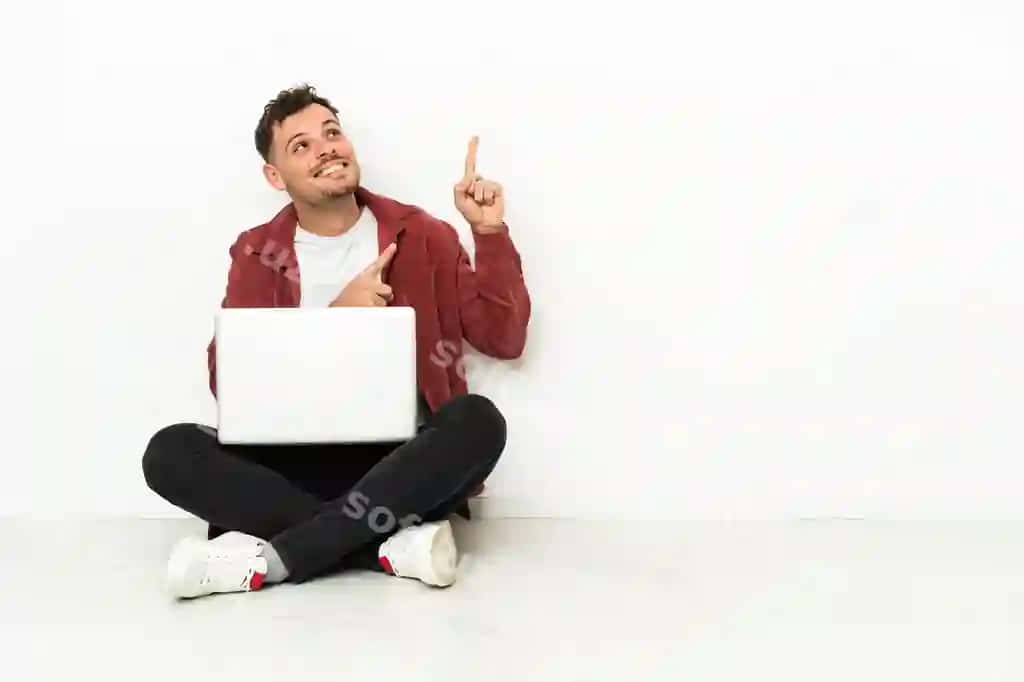 Yosh chiroyli kavkaziy erkak polga o'tirgan noutbuk bilan ko'rsatayotgan | Young handsome caucasian man sit floor with laptop pointing