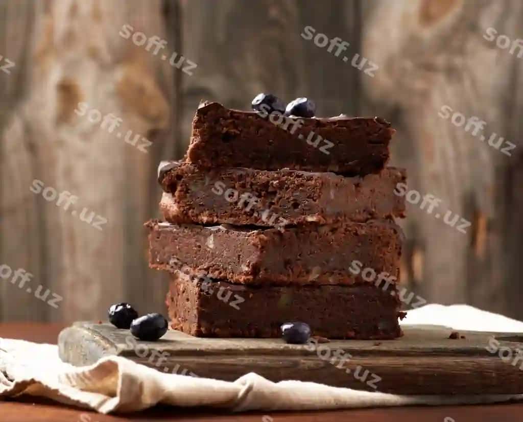 Joyiq kvadrat shaklidagi pishirilgan doyillar brownie shokoladli tort badem bilan yong'oq yuzada. | Stack square baked slices brownie chocolate cake with walnuts wooden surface