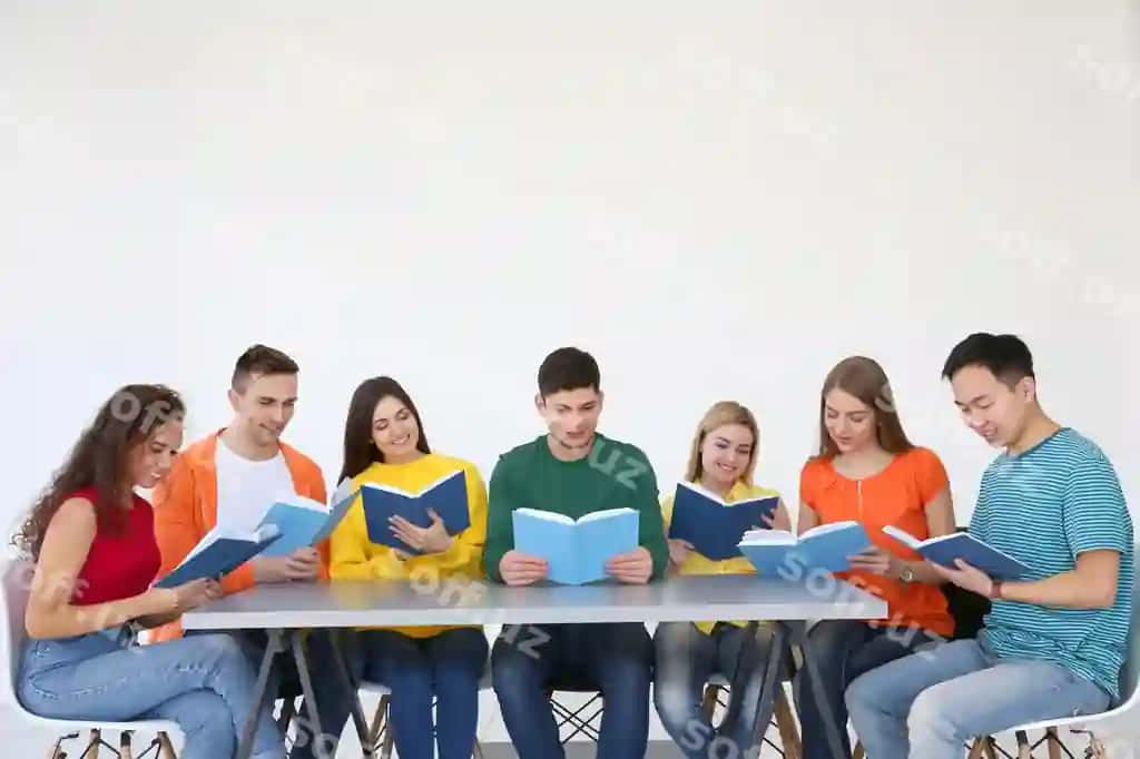Guruhda odamlar jadvalda o'tirgan holda kitob o'qiyotgan. | Group people reading books while sitting table