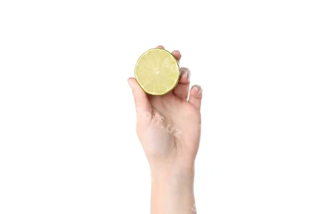 Ayol qo'l oq fonda ajratilgan limon yarasisini tutadi | Female hand holds lime half isolated white background
